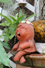 Fototapeta na wymiar A clay doll girl sitting on the edge of the tree pot.