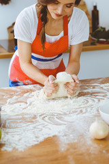 Young brunette woman cooking pizza or handmade pasta in the kitchen. Housewife preparing dough on wooden table. Dieting, food and health concept