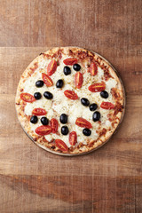 Pizza with mozzarella cheese, cherry tomatoes, black olives and oregano. Home made food. Concept for a tasty and hearty meal. Rustic wooden background. Top view. Copy space. 