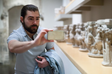 Adult male visitor using phone in sculptures exposition at museum