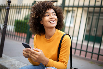 happy african american young woman holding cellphone and looking away - Powered by Adobe