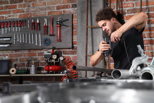 man in home workshop garage work drilling metal with drill, repair iron pipe on the workbench full of wrenches, diy and craft concept