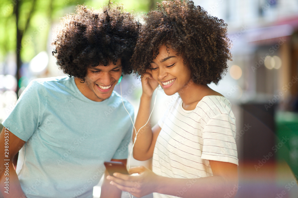 Wall mural happy african american man and woman listening to music with mobile phone and earphones