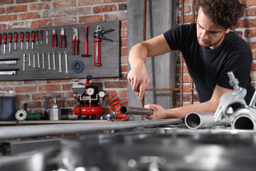 man work in home workshop garage with steel file rasp, filing metal pipe on the workbench full of...