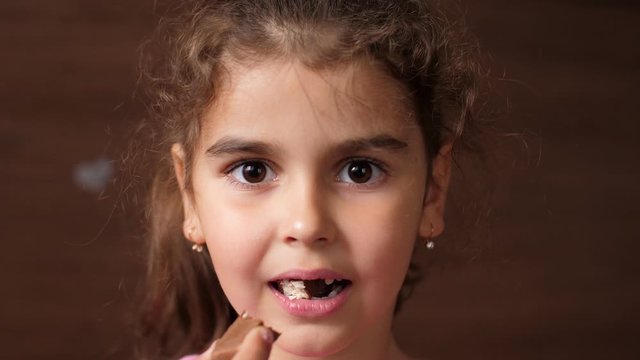 Toothless girl eats chocolate candy. A child without front teeth bites off candy. Close up