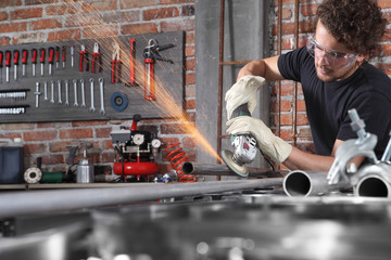 man work in home workshop garage with angle grinder, goggles and construction gloves, grinder metal...