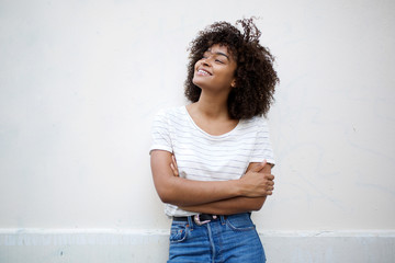 happy young african american woman smiling with arms crossed and looking away against white...