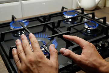 Hands of a man close-up near a gas stove. A man warms his hands by the stove due to poor heating at home. Heat inclusion season in Ukraine, Russia