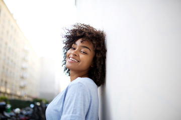 Close up beautiful smiling young african american woman leaning against wall outside