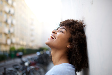 side portrait of beautiful smiling young african american woman leaning against wall outside