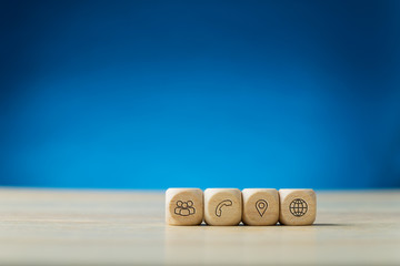 Four wooden dices with contact and information icons on them placed in a row
