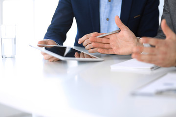 Two unknown businessmen or partners using tablet pc and discussing questions at meeting in modern office, close-up of hands. Group of managers at negotiation or brainstorm. Teamwork, partnership and