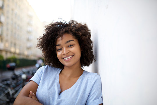smiling young african american woman leaning against wall outside