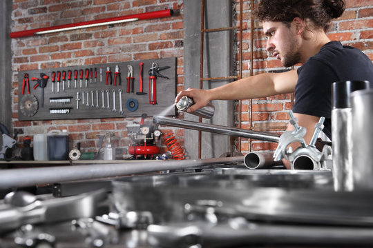 Man Work In Home Workshop Garage With Spray Can Paint Metal Pipe On The Workbench Full Of Wrenches, Diy And Craft Concept