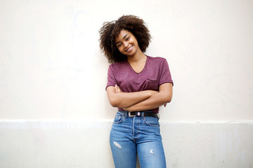 cool african american girl with arms crossed smiling by white wall