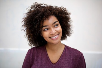 happy young african american woman with curly hair by white wall glancing