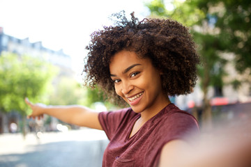 smiling young african american woman taking selfie and pointing to background