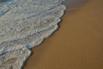 Wave of the sea entering the sand of the beach forming foam, contrast of white and beige. Macro photography