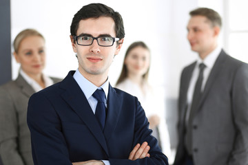 Headshot of businessman standing straight with colleagues at background in office. Group of business people discussing questions at conference or presentation. Success and business concept
