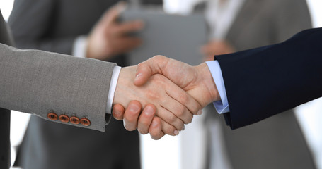 Business people shaking hands while standing with colleagues after meeting or negotiation, close-up. Group of unknown businessmen and women in modern office. Teamwork, partnership and handshake