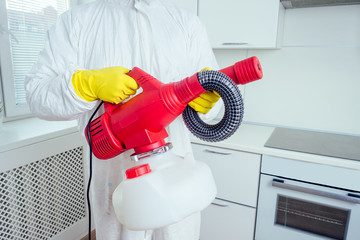 pest control worker standing with sprayer in kitchen