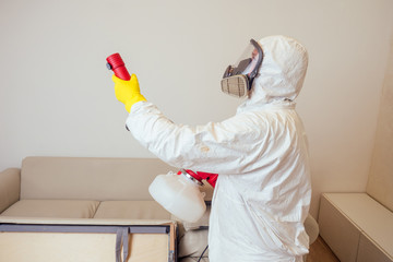 pest control worker in uniform spraying pesticides under couch in living lounge room
