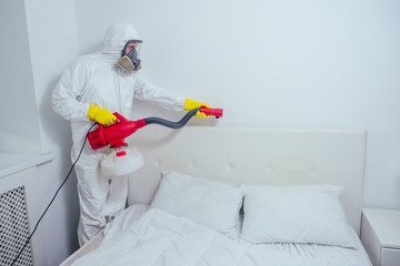 pest control worker lying on floor and spraying pesticides in bedroom