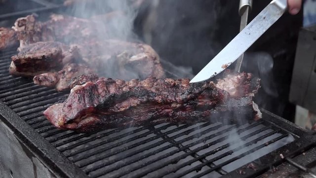 Close up on hands holding a smoked brisket on a cutting board, quickly slicing cooked meat into thin slices for a barbecue plate in a restaurant. BBQ is tender, juicy, black rim, fat rim, delicious.