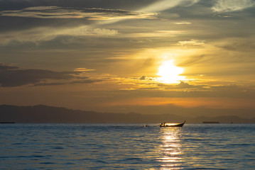Silhouette of moving long tail boat with shadow of island  and orange light of sunrise in background. Landscape of calm sea in early morning