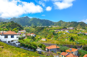 Fototapeta na wymiar Beautiful village Porto da Cruz in Madeira island, Portugal. A small city surrounded by green hills and forest. Rural buildings on a hill. Remote area, Portuguese landscapes. Tourist destination