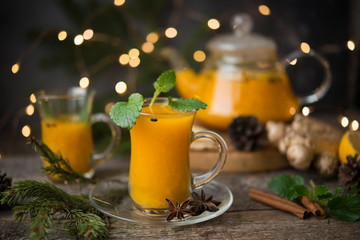 Hot winter drink of sea buckthorn with spices, served with Christmas decorations and garlands. Selective focus.