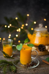 Hot winter drink of sea buckthorn with spices, served with Christmas decorations and garlands. Selective focus.