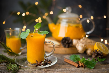 Hot winter drink of sea buckthorn with spices, served with Christmas decorations and garlands. Selective focus.