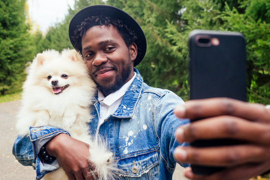 african american man making self portrait with fluffy spitz in summer spring park