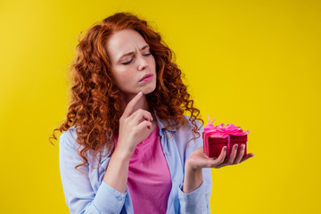 thoughtful frowning redhaired ginger curly woman holding gifts boxes and thinking dont want give it...