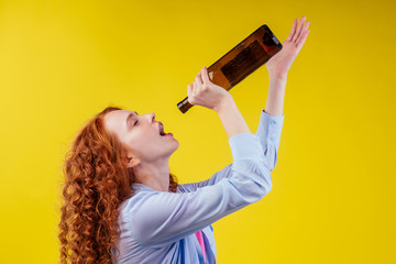 curly redhead ginger woman drinking beer and feeling bad mood in csudio yellow background