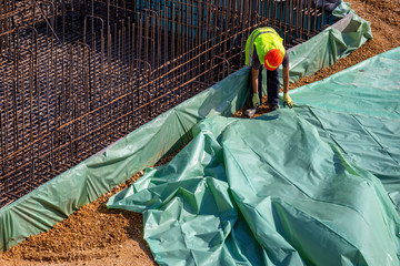 Worker installing plastic vapor barrier under concrete slab