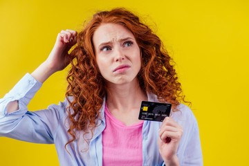 Confused redhaired ginger curly woman colding plastic creditcard and looking upsad .rejection concept
