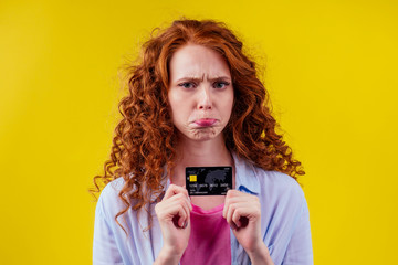 Confused redhaired ginger curly woman colding plastic creditcard and looking upsad .rejection...