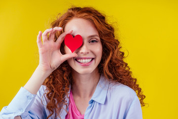 cardiologist redhaired ginger curls happy woman holding paper heard in studio yellow background