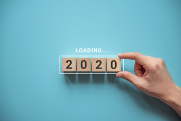 Loading new year 2020 with hand putting wood cube in progress bar.