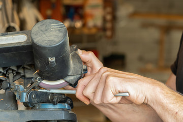 man hands cutting metal rod in a machine with abrasive disck in a workshop