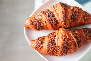 Top view of plate of freshly baked croissants with chocolate chips in a white plate on a glass table in the living room.