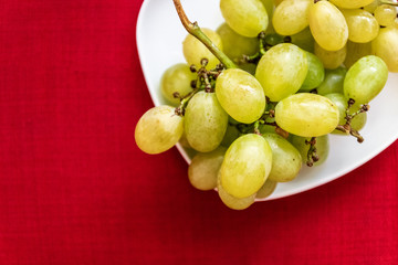 Big tasty sweet grapes on a white plate on a red background