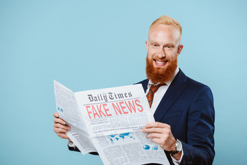 smiling bearded businessman reading newspaper with fake news, isolated on blue