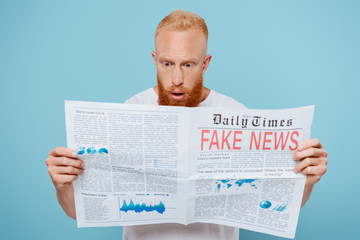 shocked bearded man reading newspaper with fake news, isolated on blue