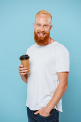 smiling bearded man in t-shirt holding coffee to go, isolated on blue