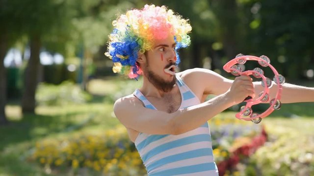 Crazy mime dancing with a tambourine in the park. Funny antics and sketch of a clown on the street.