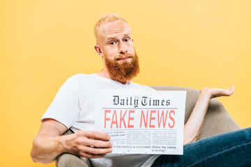 skeptical man reading newspaper with fake news while sitting on armchair with shrug gesture, isolated on yellow