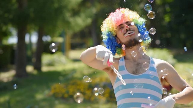 Mime blows soap bubbles in the park. Clown shows a sketch in the street.